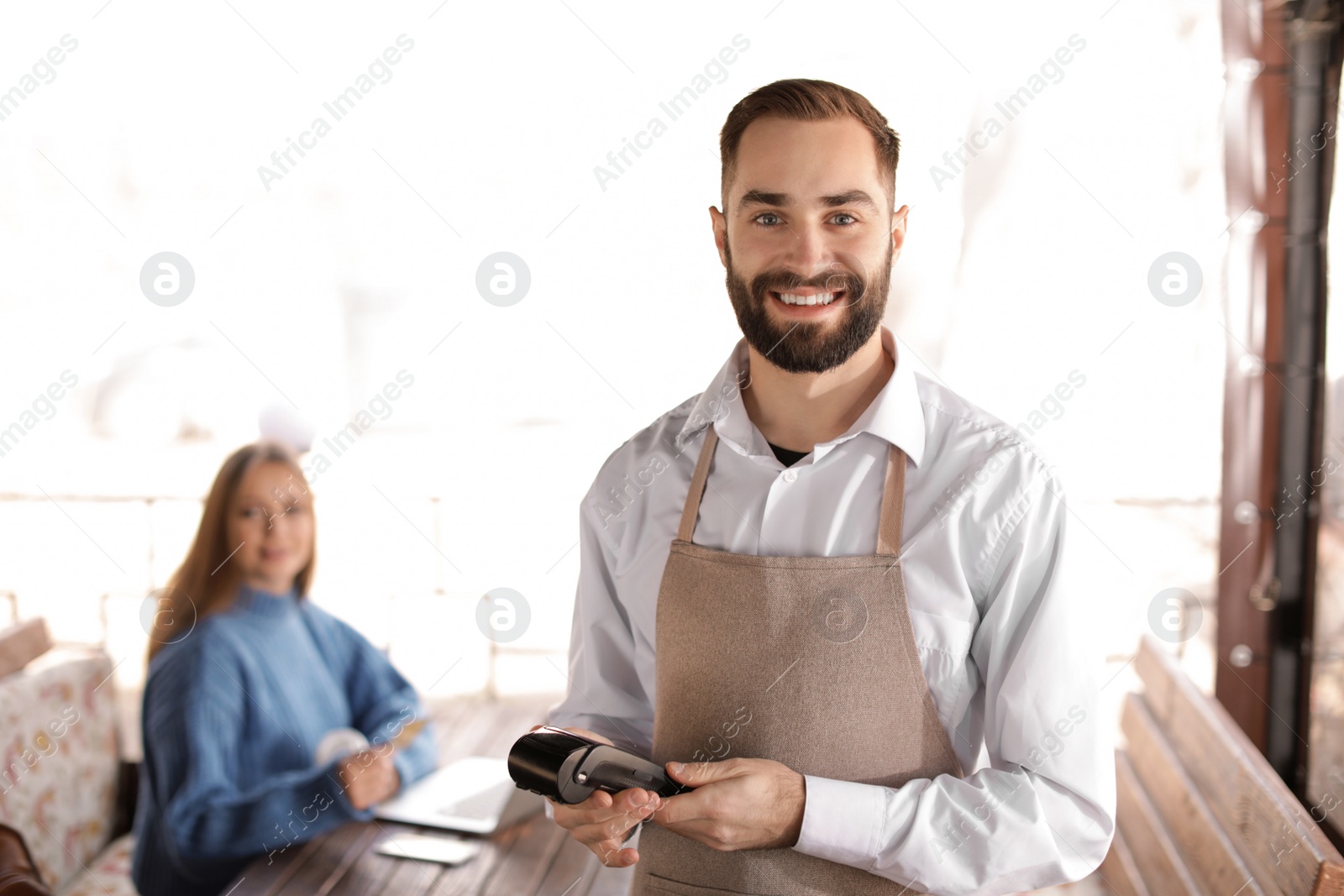 Photo of Waiter holding payment terminal near table with client at restaurant