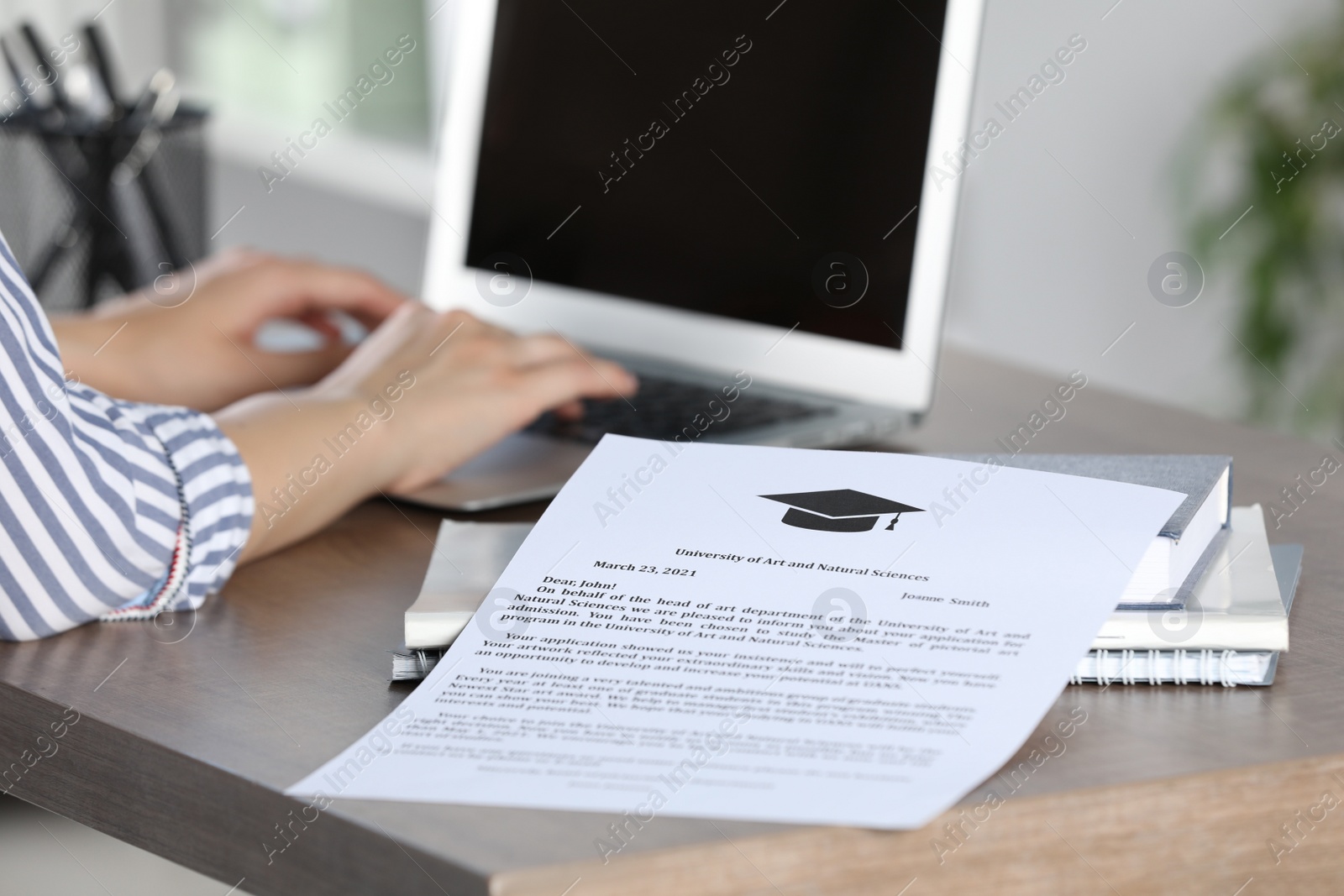 Photo of Student working with laptop at table indoors, focus on acceptance letter from university