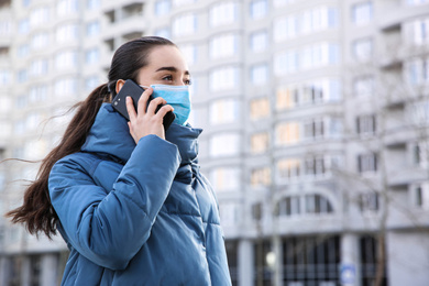 Woman with disposable mask talking on phone outdoors. Dangerous virus