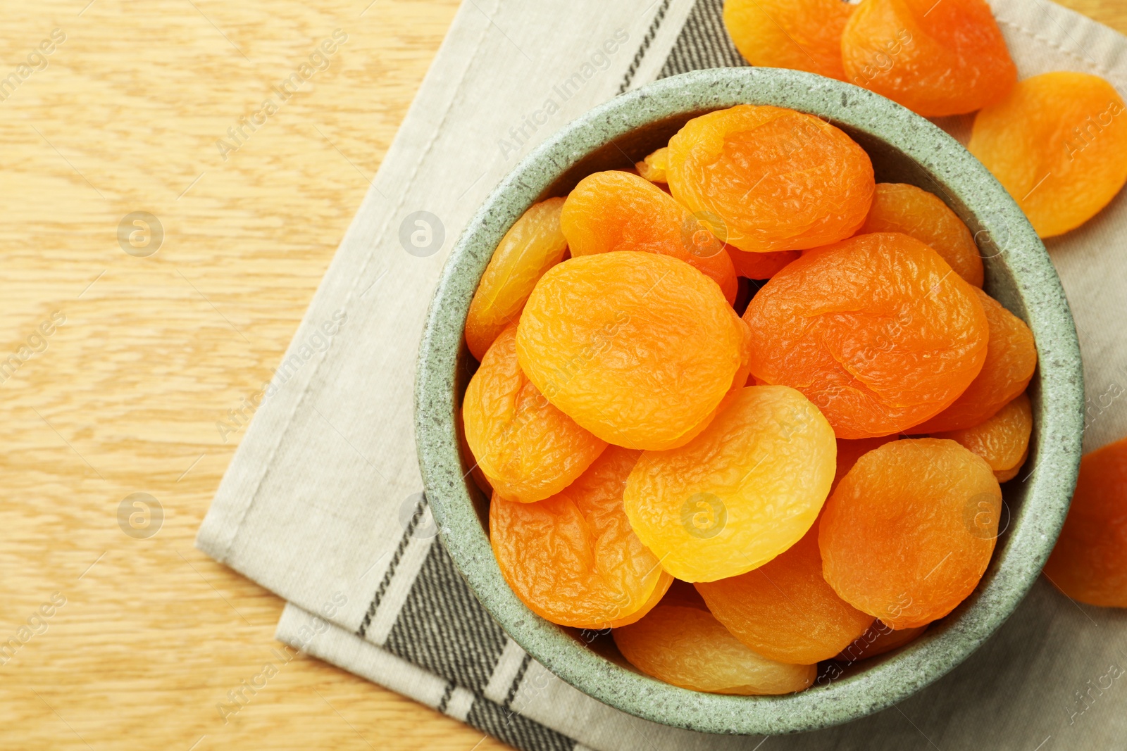 Photo of Bowl of tasty apricots on wooden table, top view and space for text. Dried fruits