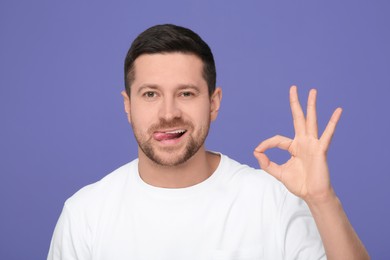 Photo of Happy man showing his tongue and OK gesture on purple background