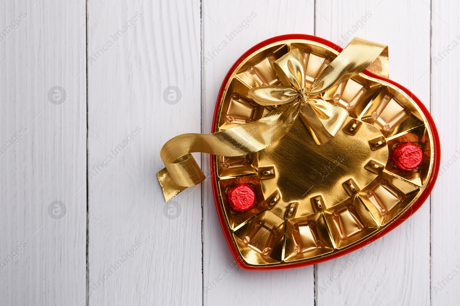 Photo of Partially empty box of chocolate candies on white wooden table, top view. Space for text