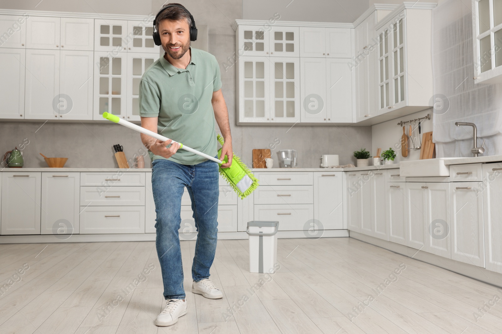 Photo of Enjoying cleaning. Happy man with mop singing while tidying up in kitchen. Space for text