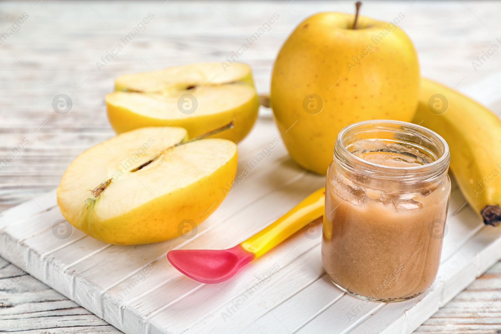 Photo of Jar with healthy baby food and apple on wooden board