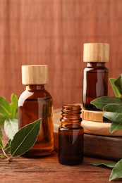 Photo of Bottles of bay essential oil and fresh leaves on wooden table