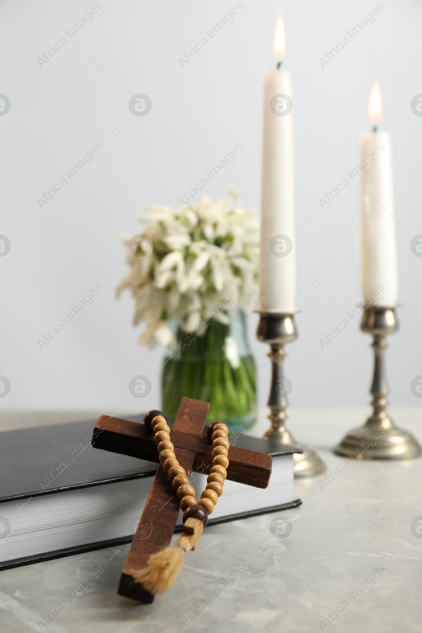 Photo of Wooden cross, rosary beads, Bible, church candles and flowers on marble table