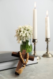 Wooden cross, rosary beads, Bible, church candles and flowers on marble table