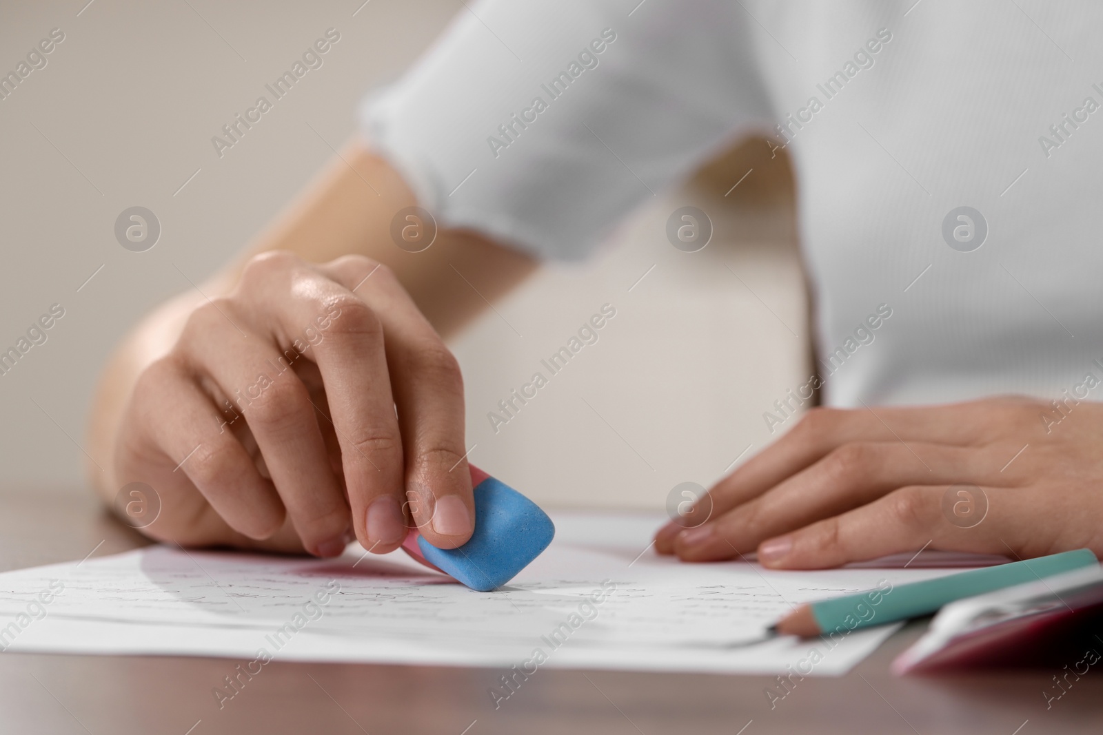 Photo of Girl erasing mistake in her notebook at wooden desk, closeup