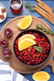 Photo of Cranberries in bowl, jars with sauce and ingredients on blue wooden table, flat lay