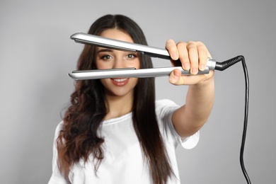 Photo of Happy woman with hair iron on grey background