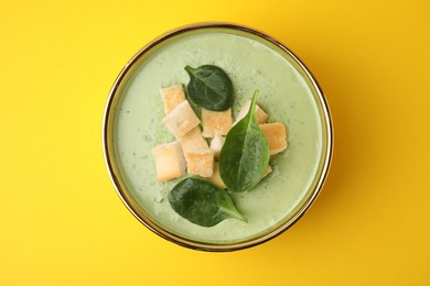 Photo of Delicious spinach cream soup with croutons in bowl on yellow background, top view