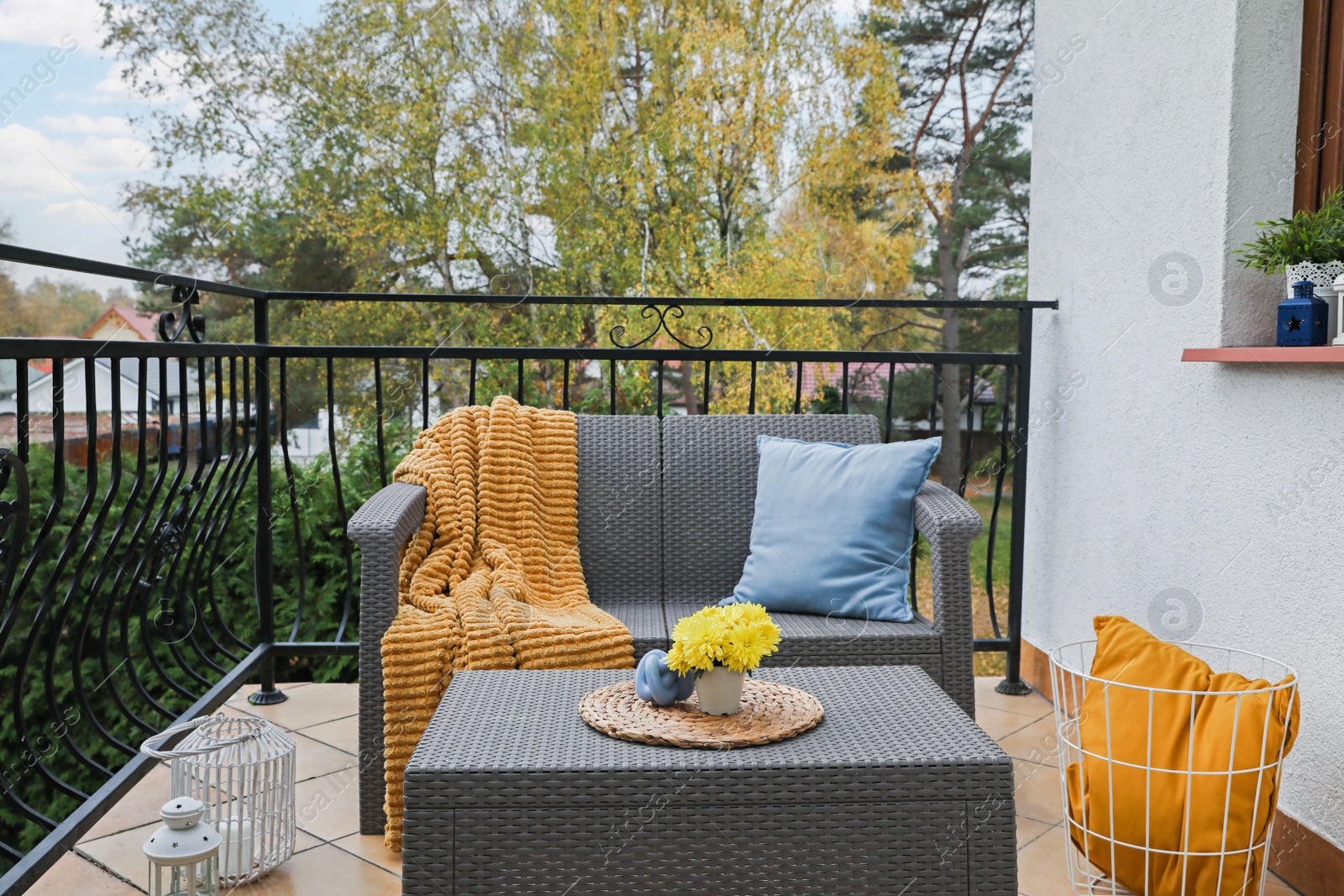 Photo of Colorful pillows, soft blanket and yellow chrysanthemum flowers on rattan garden furniture outdoors