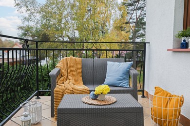 Colorful pillows, soft blanket and yellow chrysanthemum flowers on rattan garden furniture outdoors