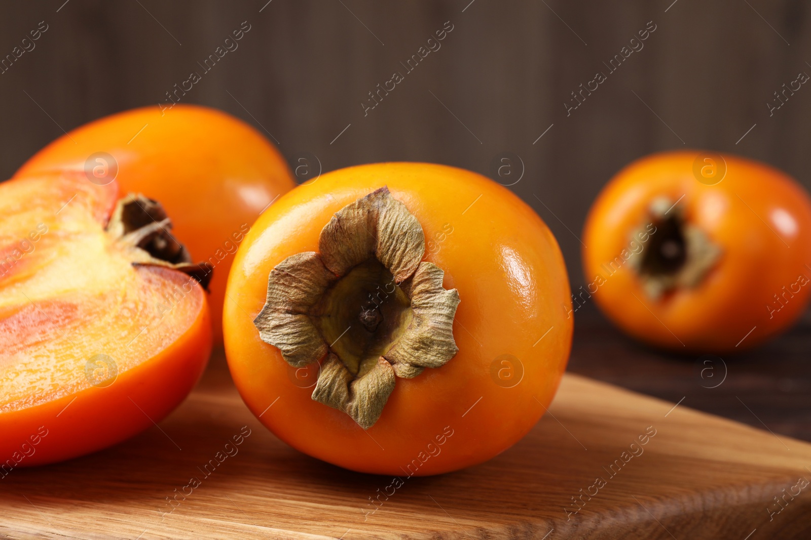 Photo of Whole and cut delicious ripe persimmons on wooden table, closeup