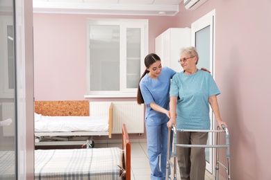 Nurse assisting senior patient with walker in hospital ward