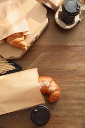 Paper bags with pastry and takeaway food on wooden table, top view. Space for text