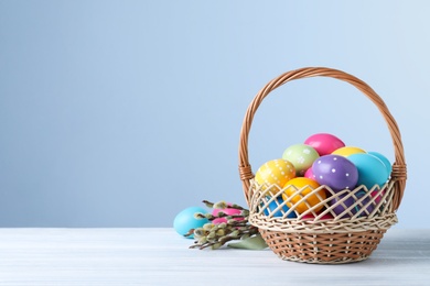Photo of Colorful Easter eggs in wicker basket and willow branches on white wooden table. Space for text