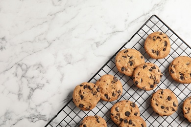 Photo of Cooling rack with chocolate chip cookies on marble background, top view. Space for text