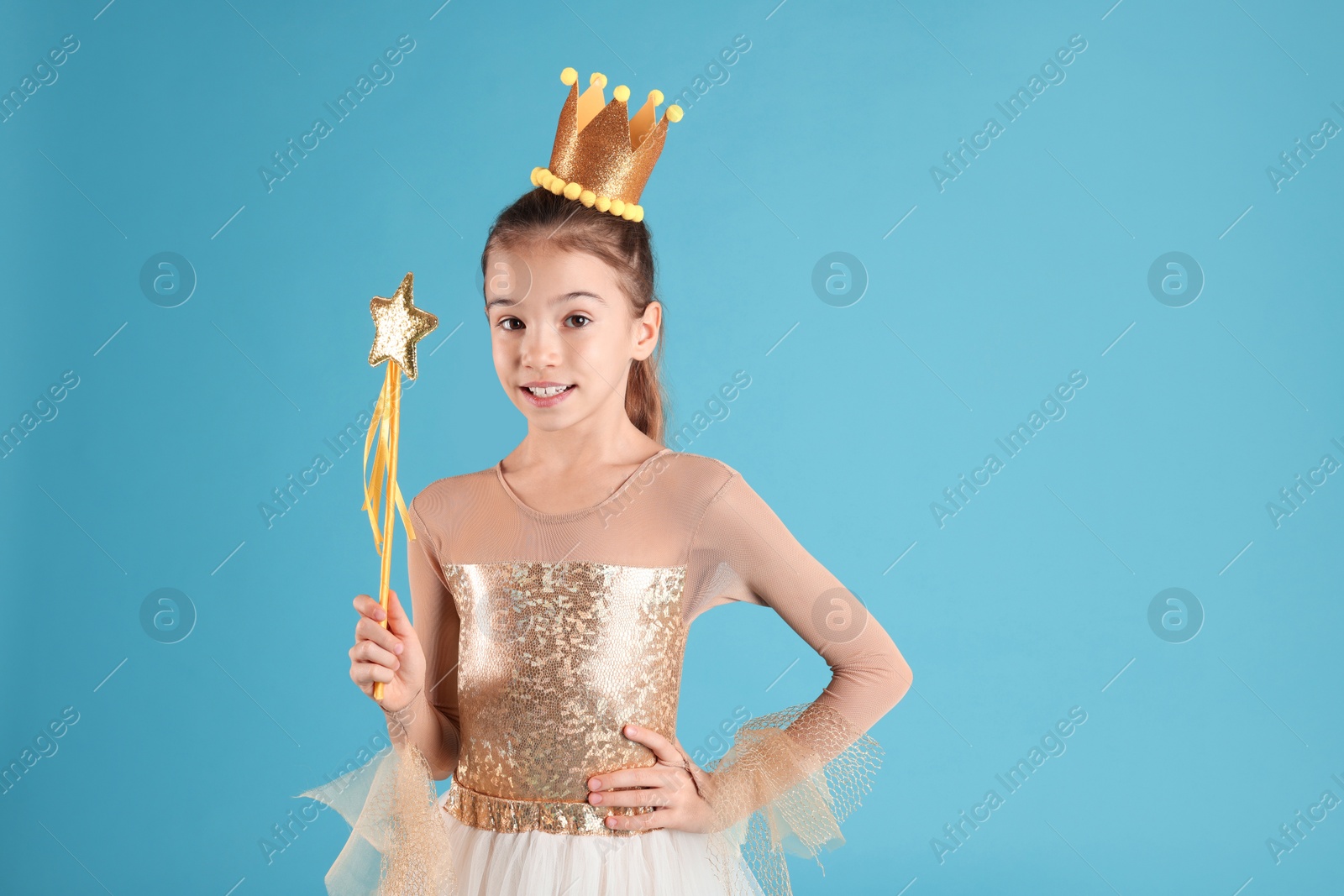 Photo of Cute girl in fairy dress with golden crown and magic wand on light blue background. Little princess