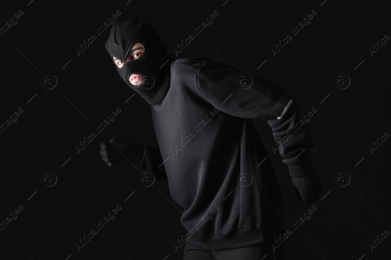 Photo of Thief in balaclava sneaking on black background