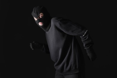Thief in balaclava sneaking on black background
