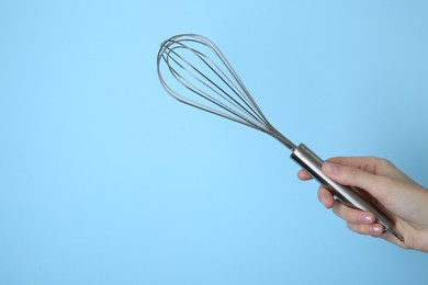 Photo of Woman holding metal whisk on light blue background, closeup. Space for text