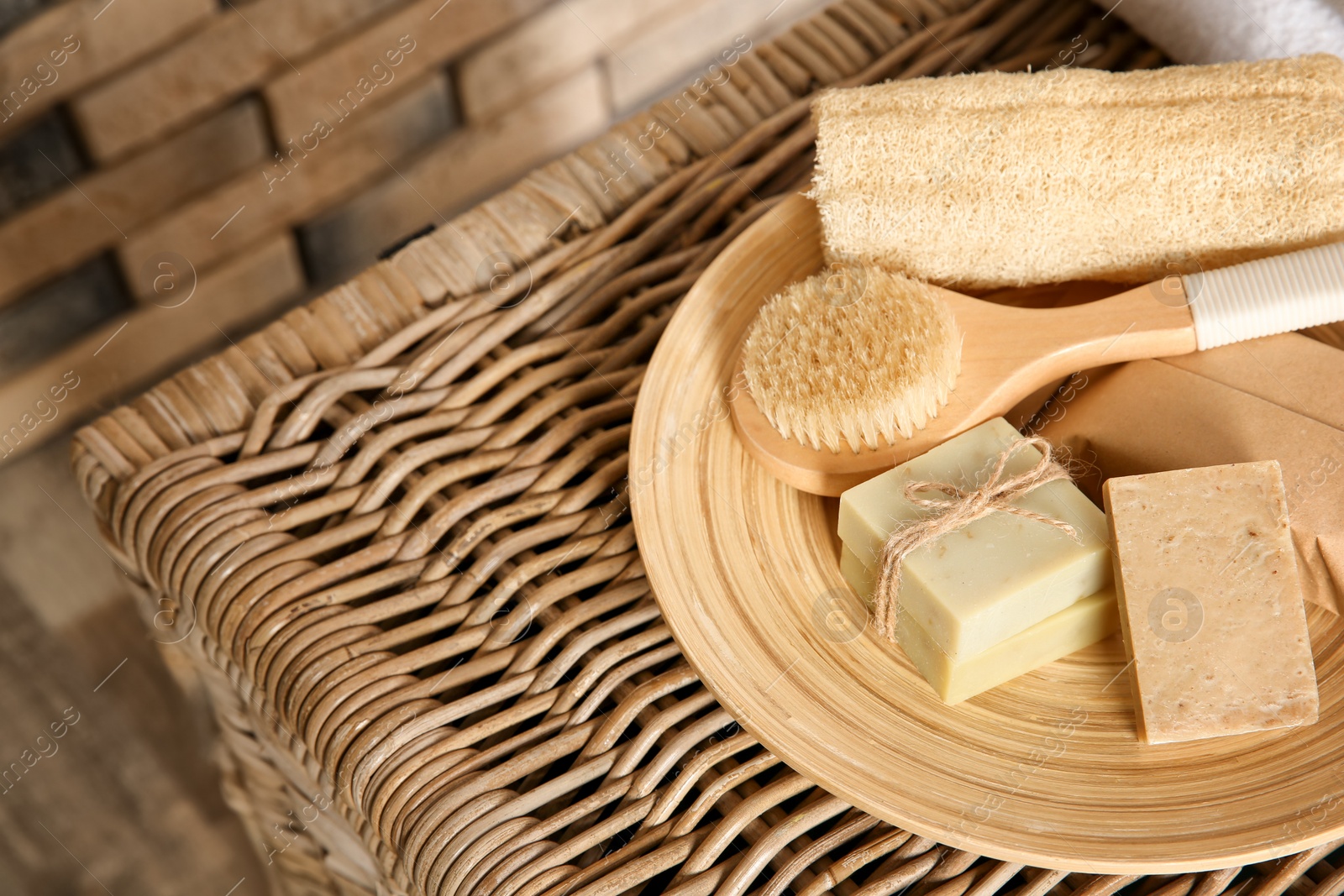 Photo of Plate with brush, wisp and handmade soap bars on wicker chest, closeup. Space for text