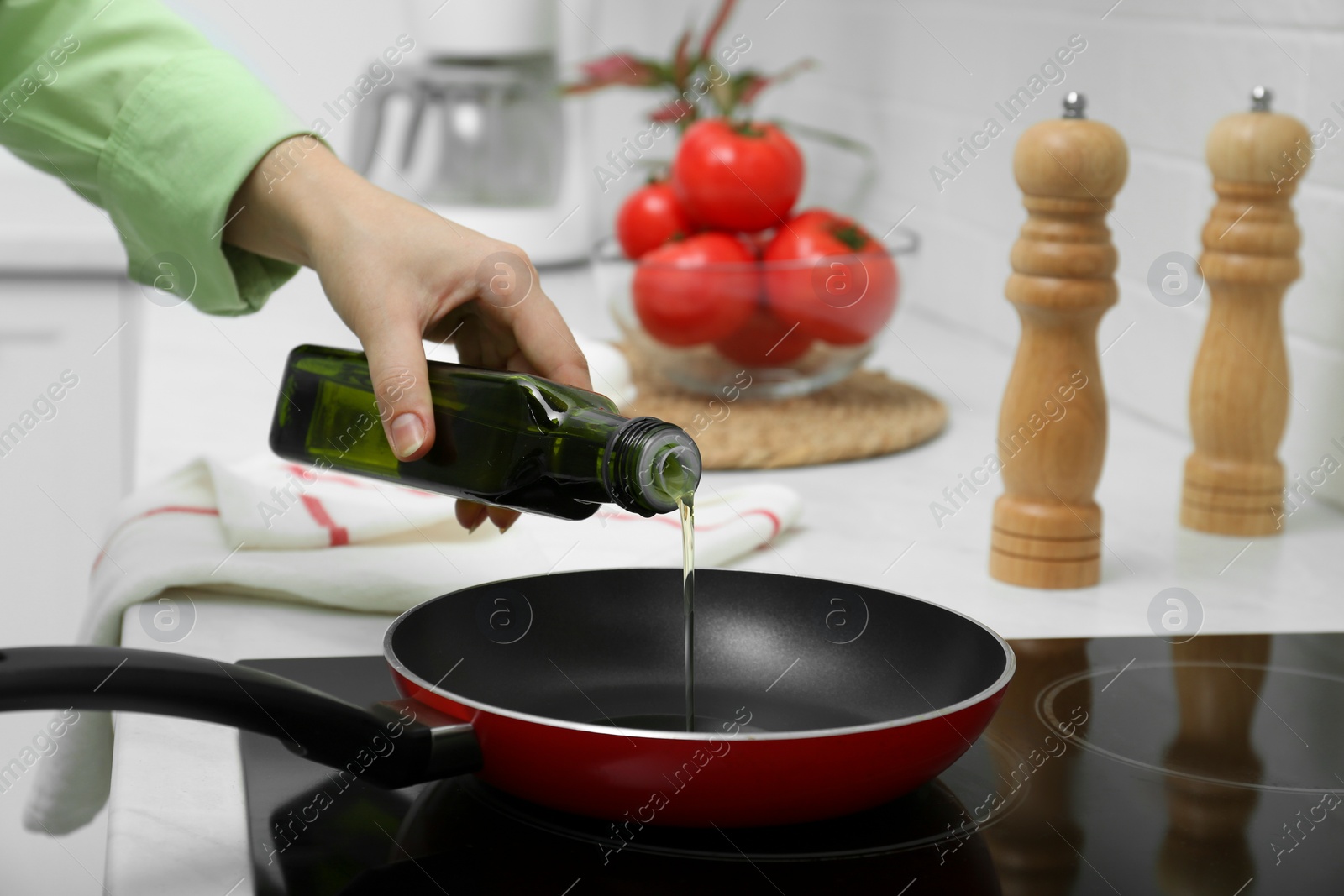 Photo of Woman pouring cooking oil from bottle into frying pan in kitchen, closeup