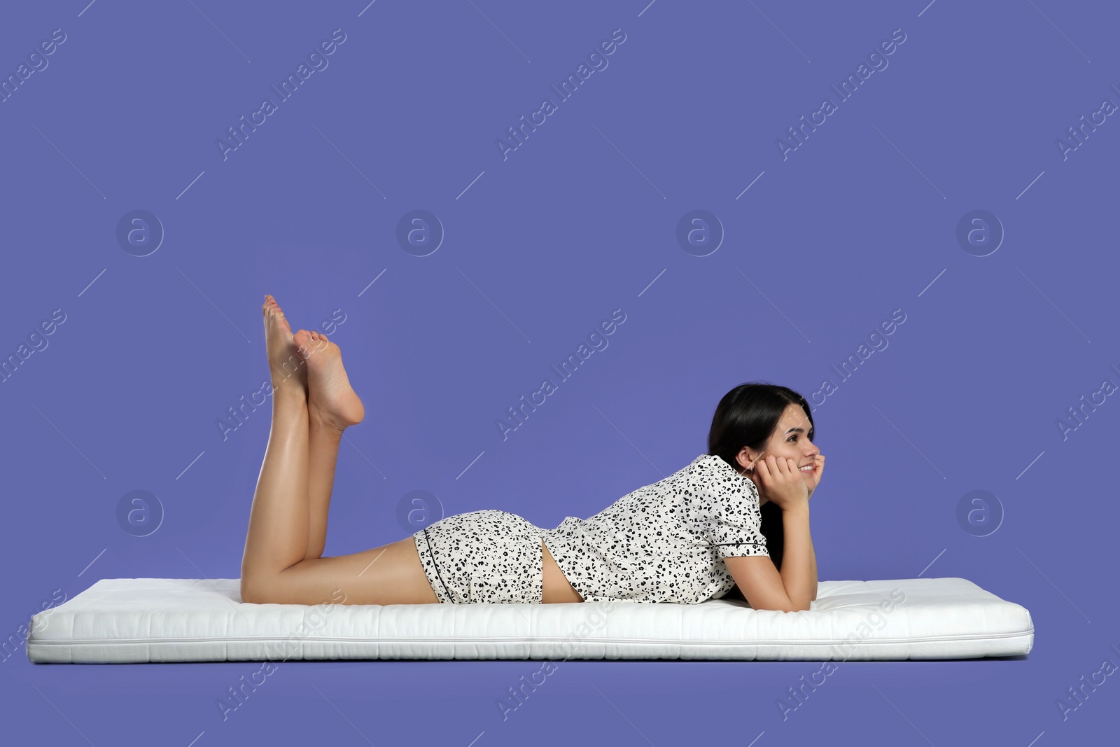 Photo of Young woman lying on soft mattress against light purple background