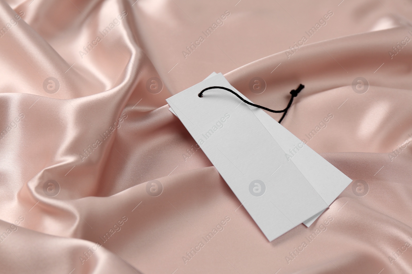Photo of Blank white tags on pink silky fabric. Space for text