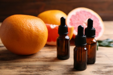 Photo of Bottles of essential oil and grapefruits on wooden table, space for text