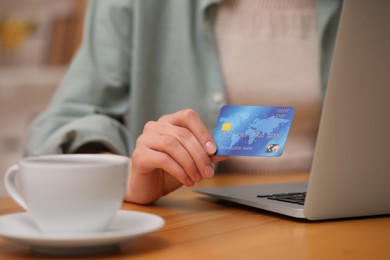 Photo of Woman with credit card using laptop for online shopping at wooden table, closeup