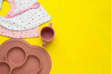 Photo of Flat lay composition with baby feeding accessories and bibs on yellow background, space for text