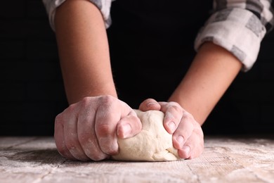 Photo of Man kneading dough at wooden table on dark background, closeup