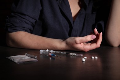 Photo of Addicted woman at table with different drugs, closeup