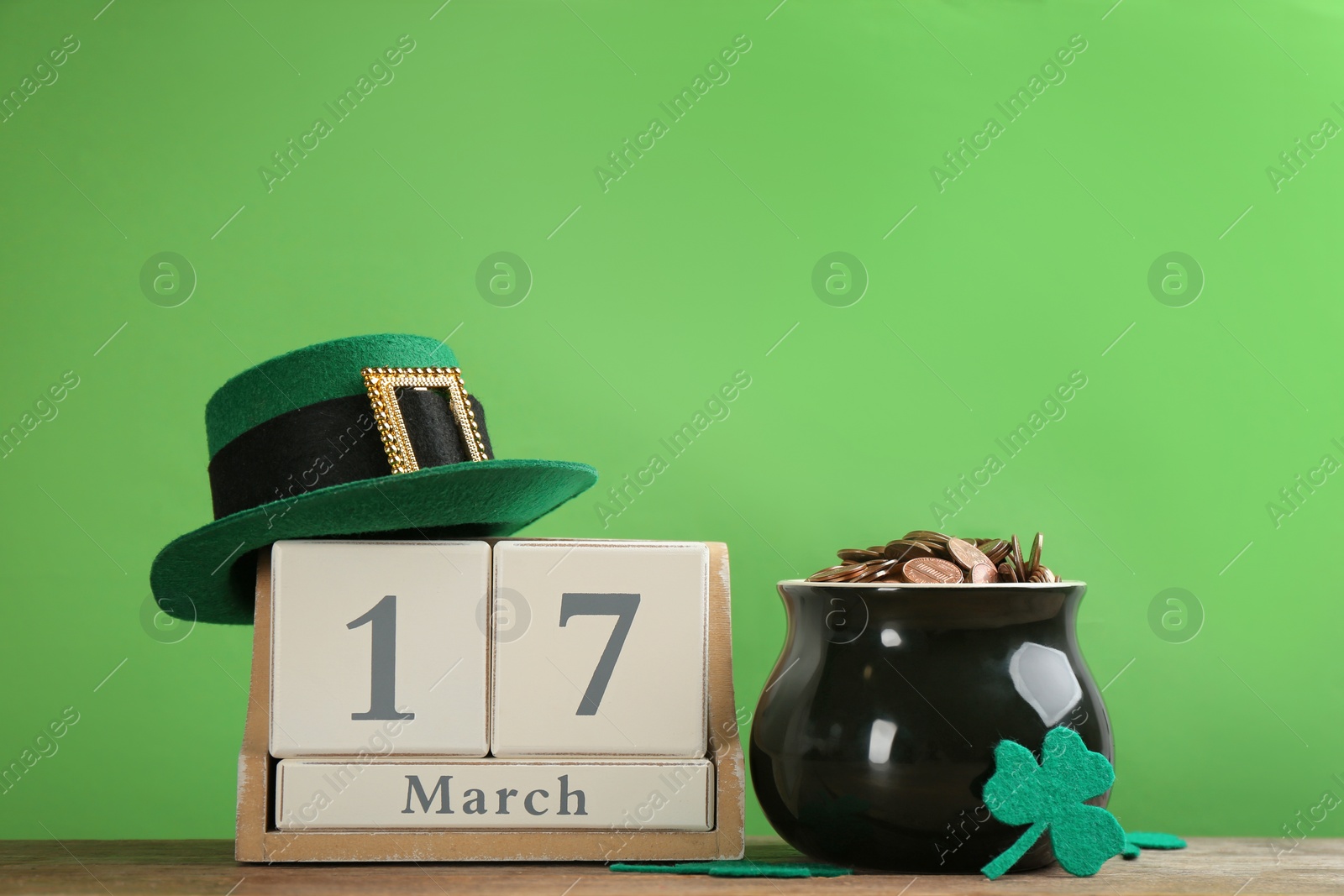 Photo of Composition with pot of gold coins and wooden block calendar on table against green background. St. Patrick's Day celebration