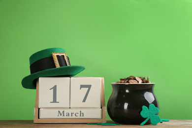 Photo of Composition with pot of gold coins and wooden block calendar on table against green background. St. Patrick's Day celebration