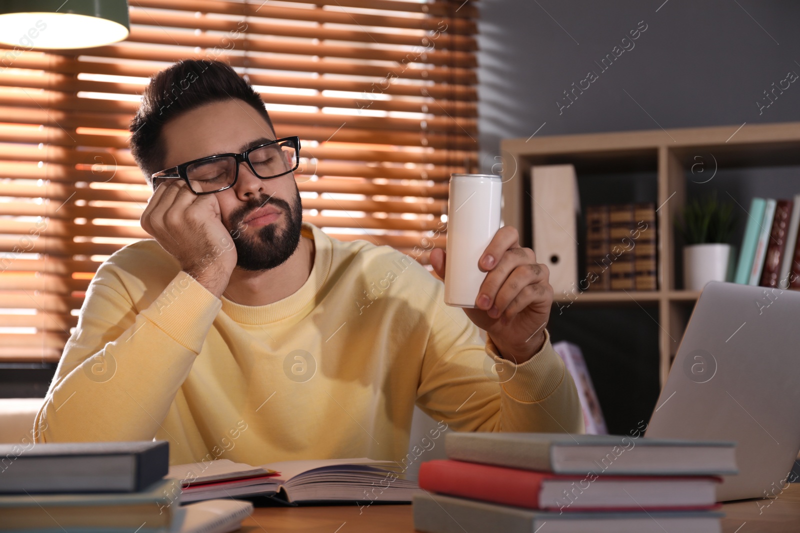 Photo of Tired young man with energy drink studying at home