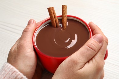 Photo of Woman holding cup of yummy hot chocolate with cinnamon on light background, closeup