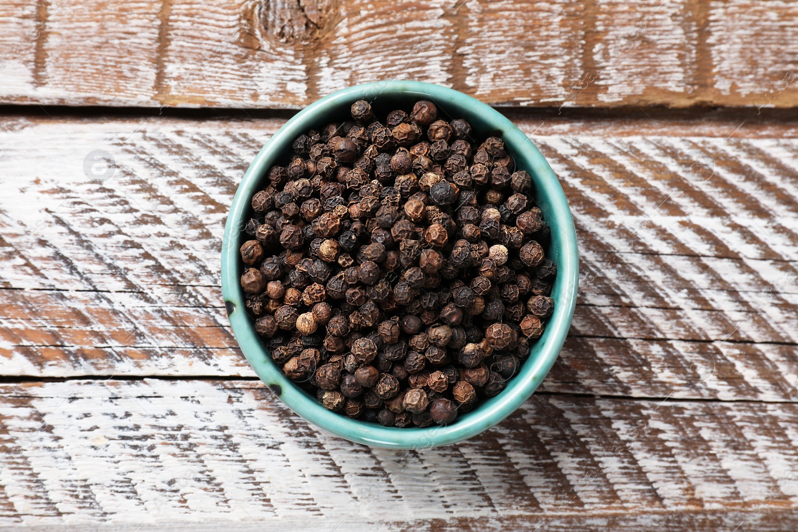 Photo of Aromatic spice. Black pepper in bowl on wooden table, top view