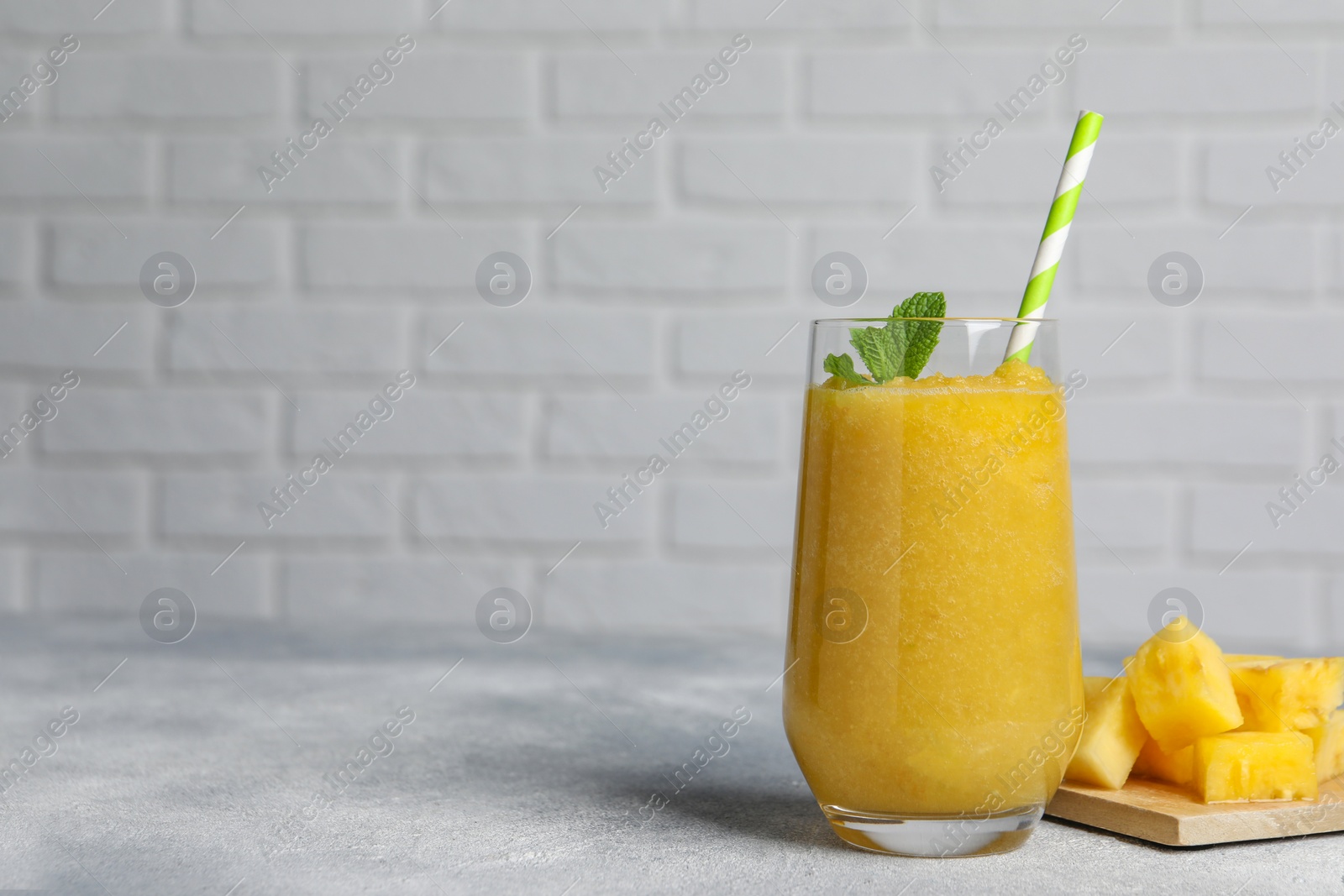 Photo of Glass of tasty pineapple smoothie and cut fruit on light gray table, space for text