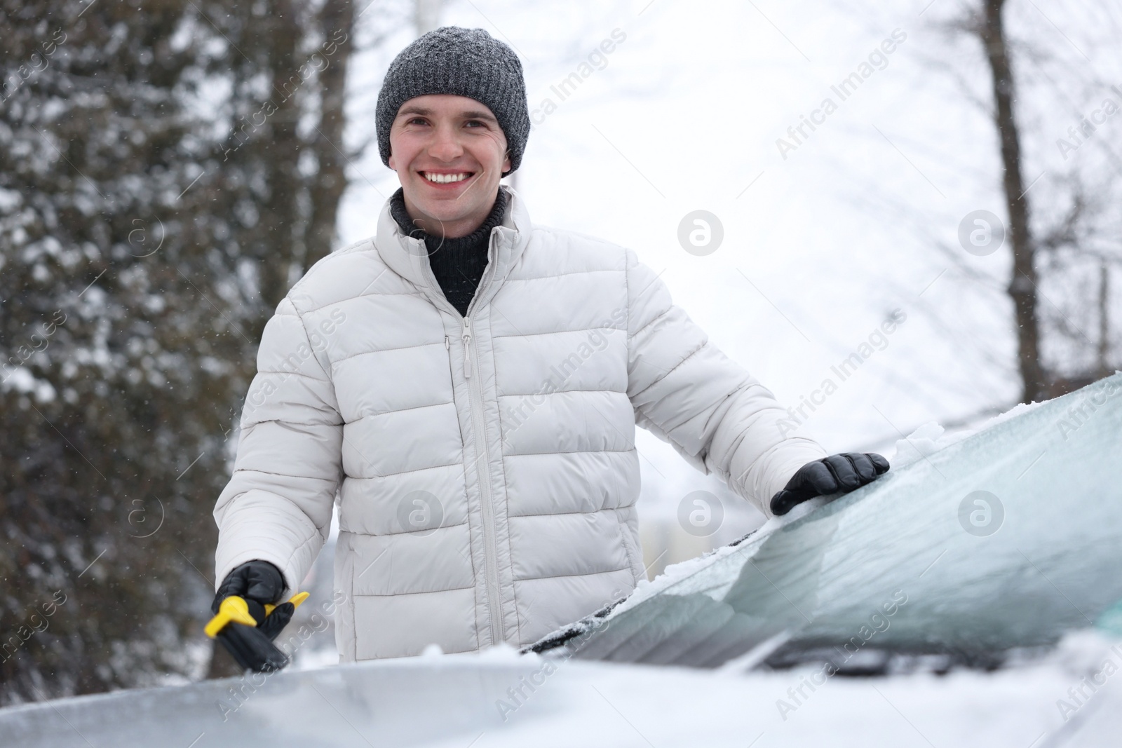 Photo of Man cleaning snow from car hood outdoors