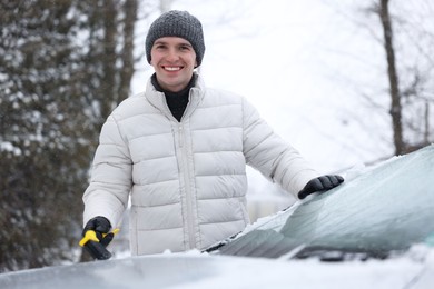 Man cleaning snow from car hood outdoors