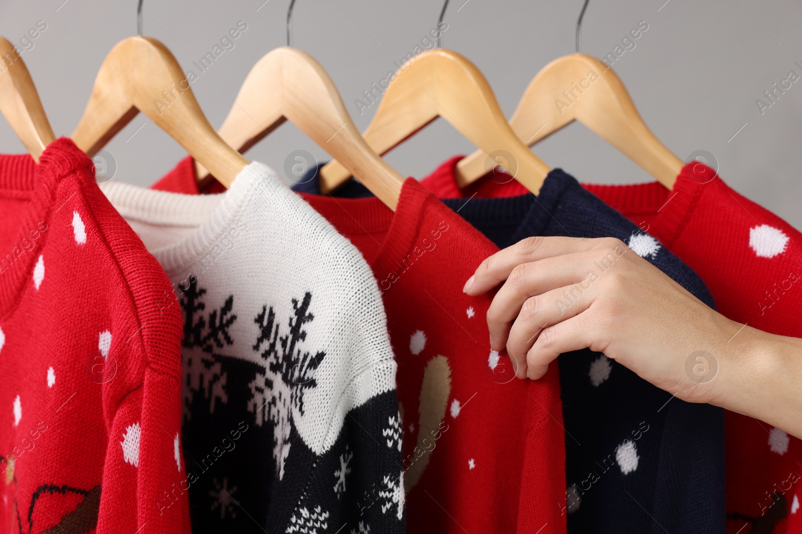 Photo of Woman choosing Christmas sweater from rack near light wall, closeup