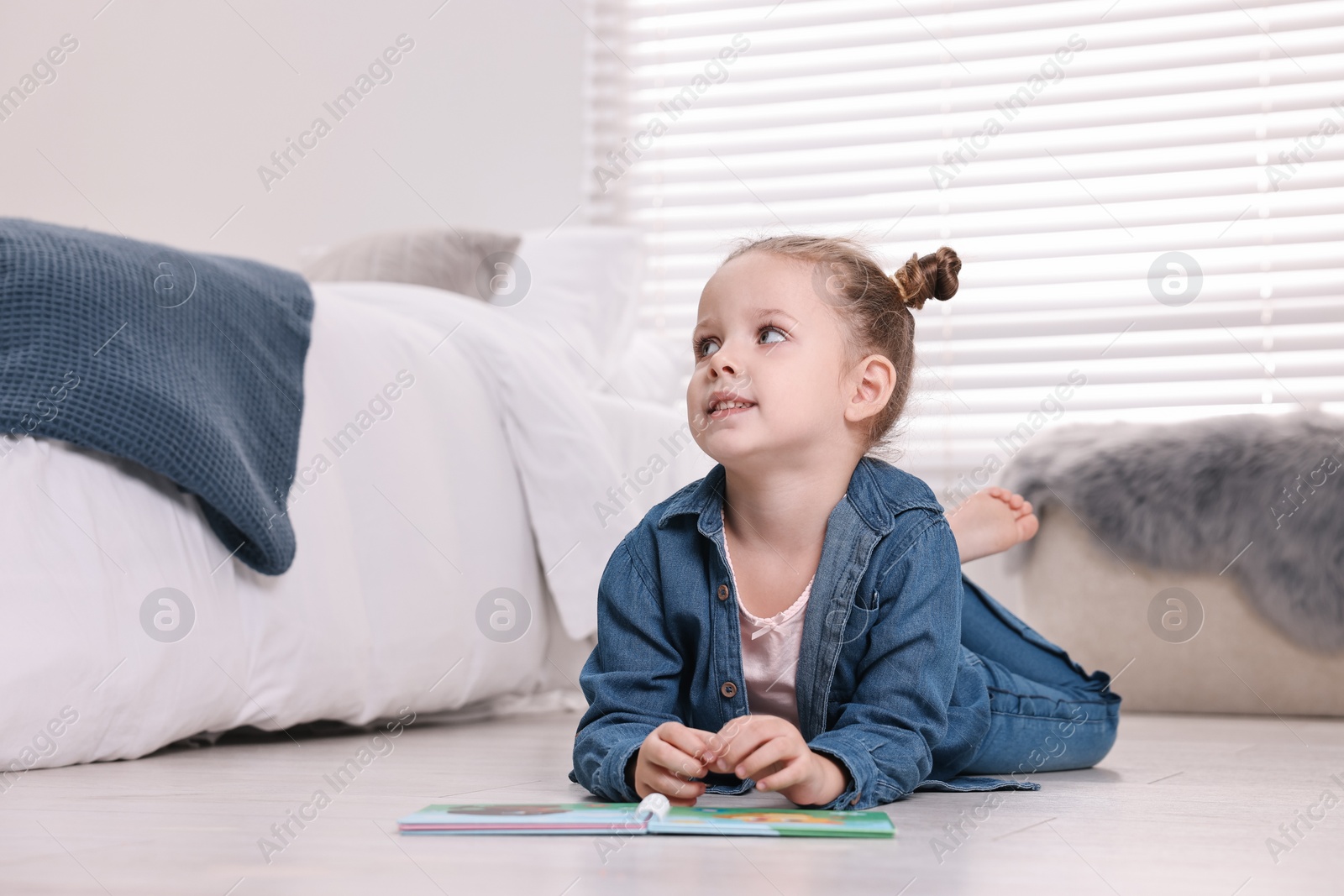 Photo of Cute little girl with book on warm floor at home, space for text. Heating system