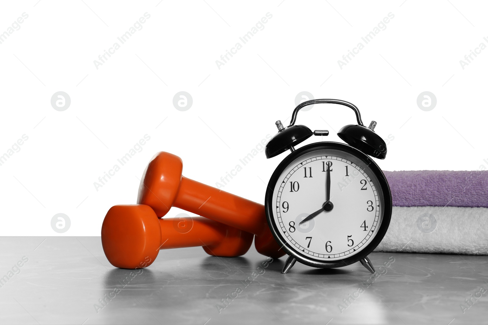 Photo of Alarm clock, towels and dumbbells on marble table against grey background. Morning exercise