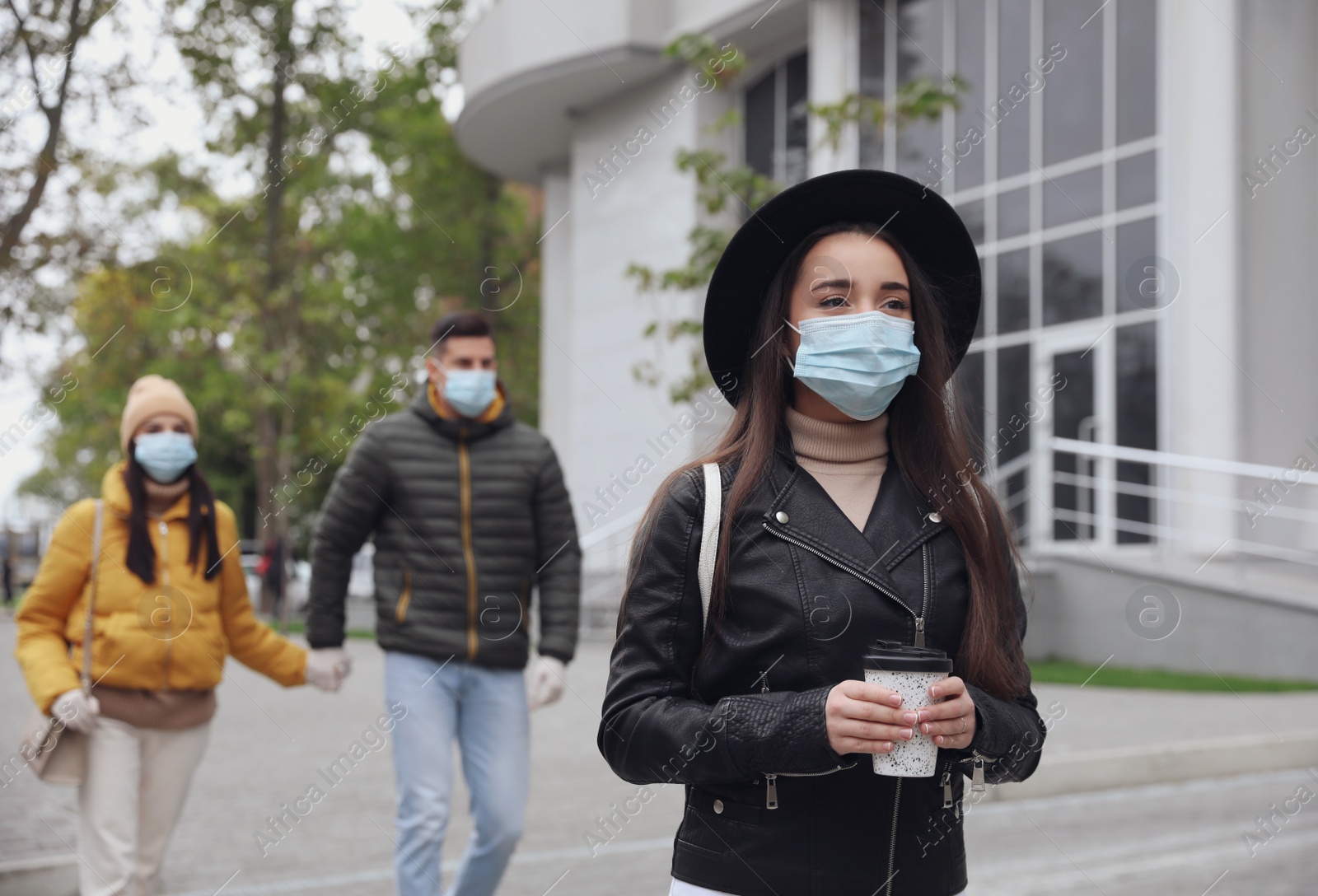 Photo of Young woman in medical face mask with cup of coffee walking outdoors. Personal protection during COVID-19 pandemic