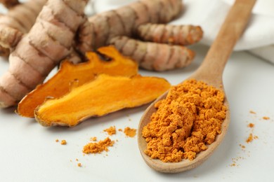 Photo of Wooden spoon with aromatic turmeric powder and raw roots on white table, closeup