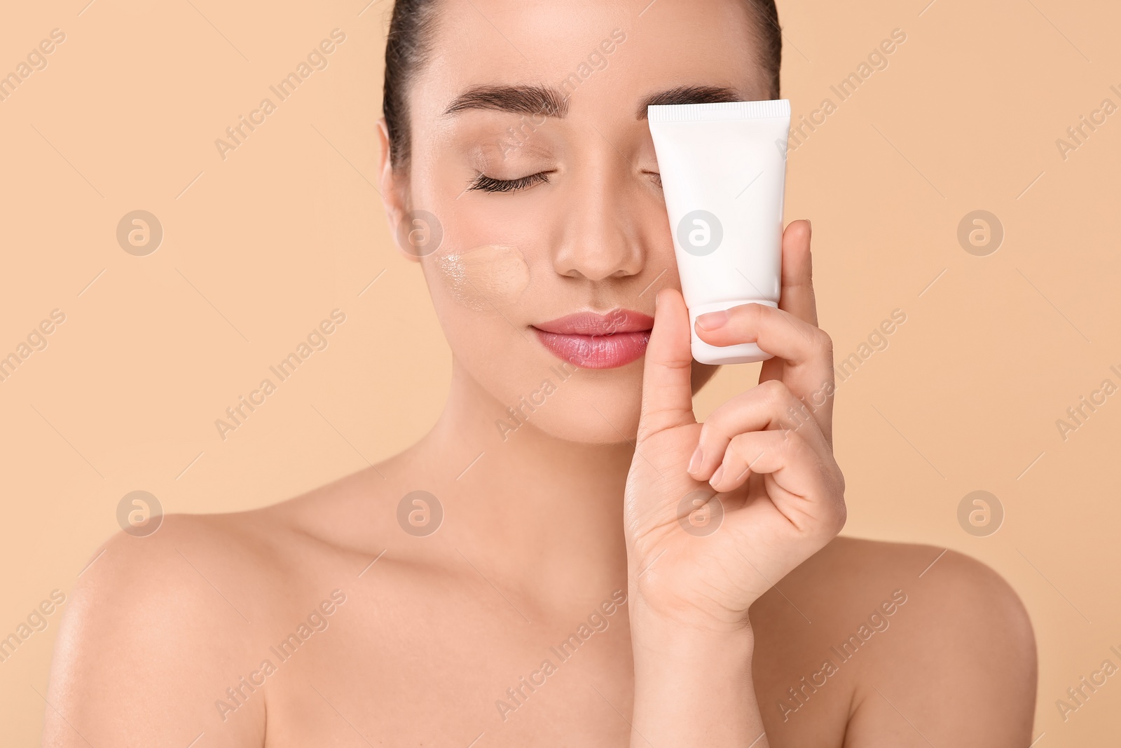 Photo of Woman holding tube of foundation on beige background