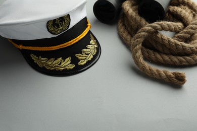 Photo of Peaked cap, rope and binoculars on light grey background. Space for text